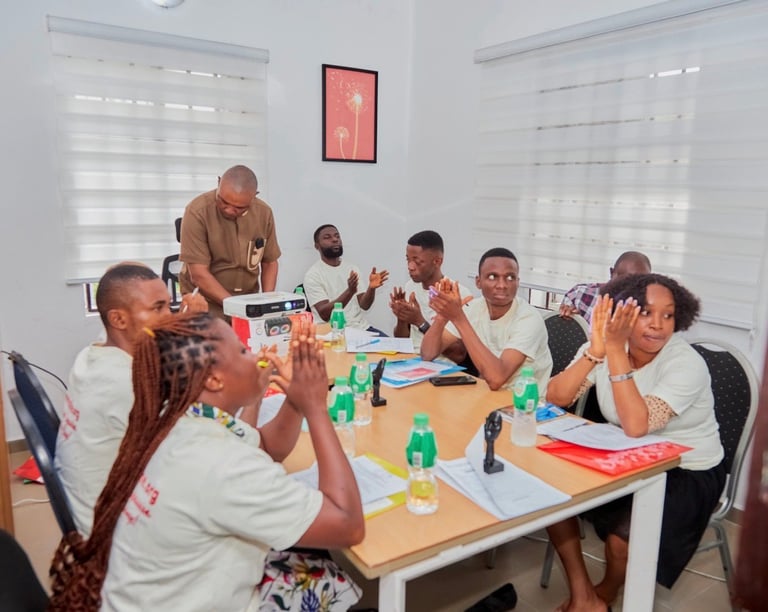 Group of people in a bright office room clapping and celebrating together around a wooden table with refreshments