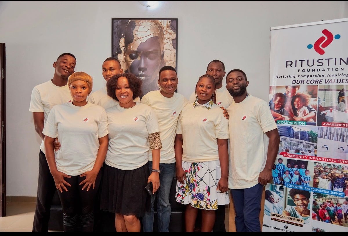 Team of eight people wearing matching cream-colored t-shirts posing together in front of Ritustin banner