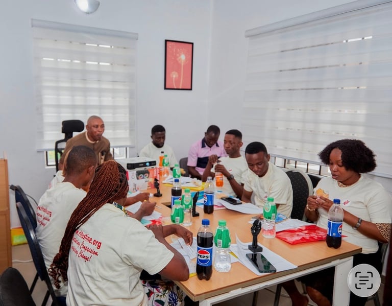 Group of people eating and socializing together at a long wooden table in a bright, modern dining space with windows